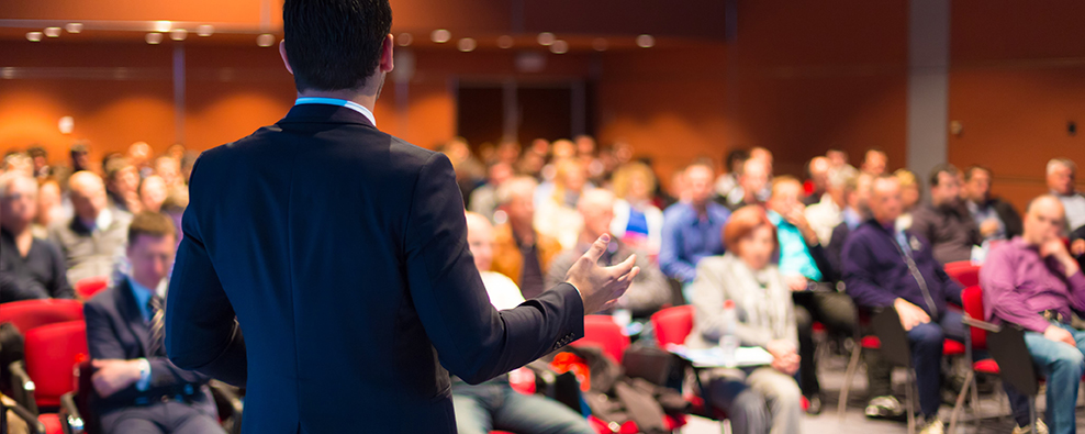 Image of a speaker before a seated audience