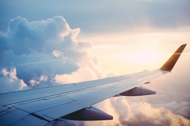 This is an image of an airplane in flight, seen from the point of view of a passenger looking out their window and seeing the rays of the sun reflect on the wing of the plane as it passes through the clouds.