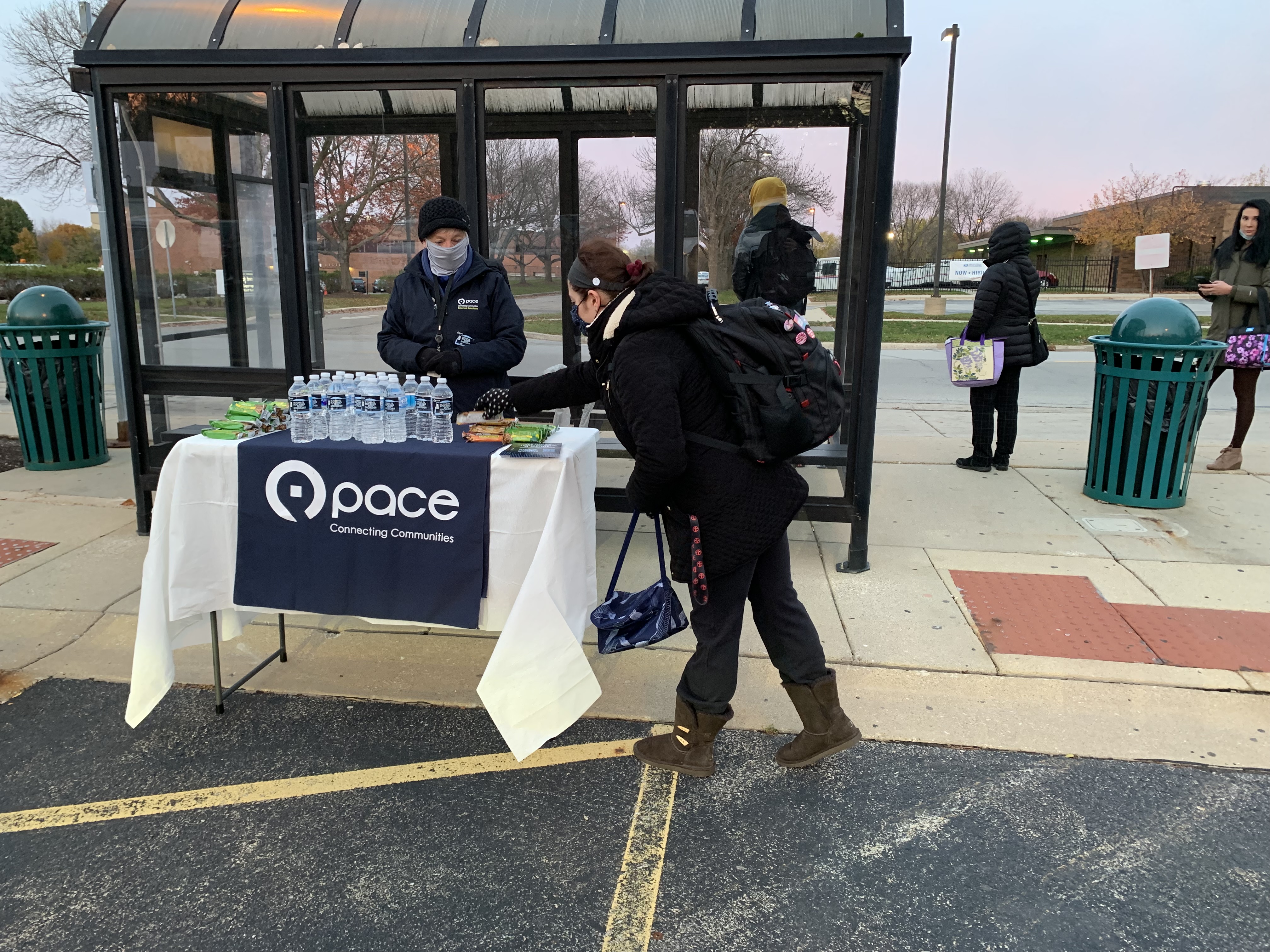 person takes a granola bar off a display table at a Pace bus stop