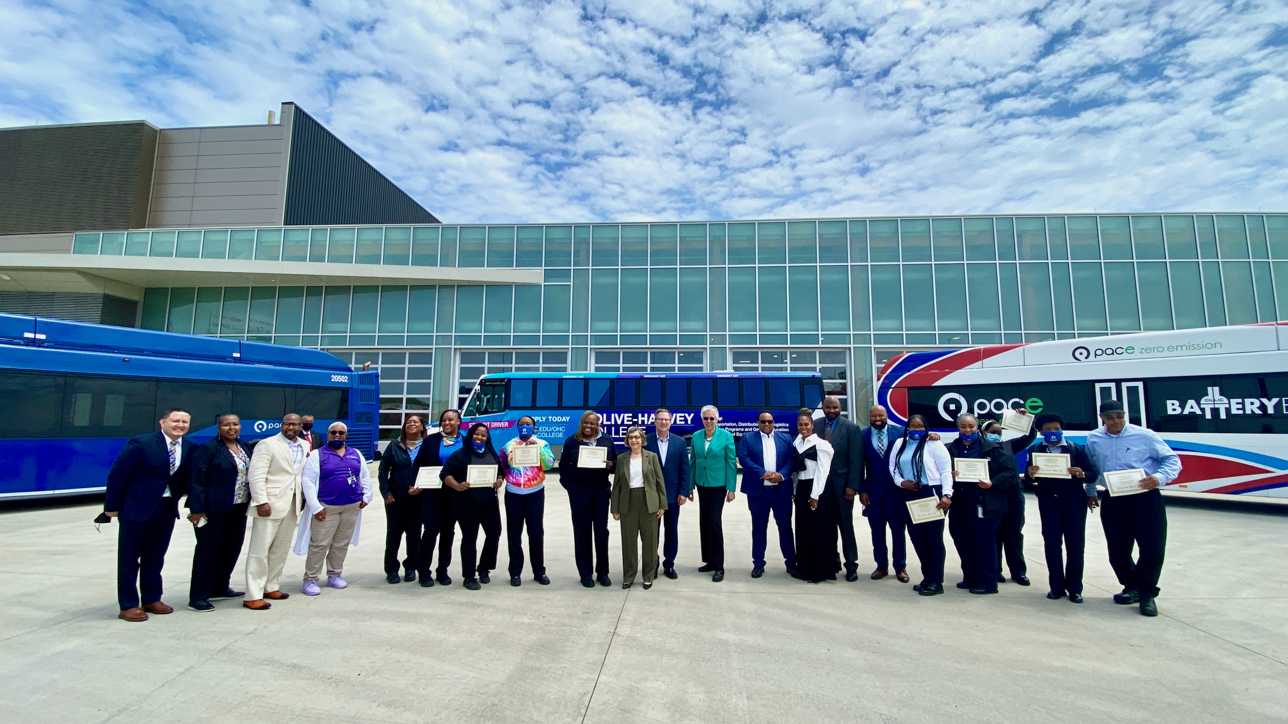 officials pose in front of buses with graduates showing their diplomas