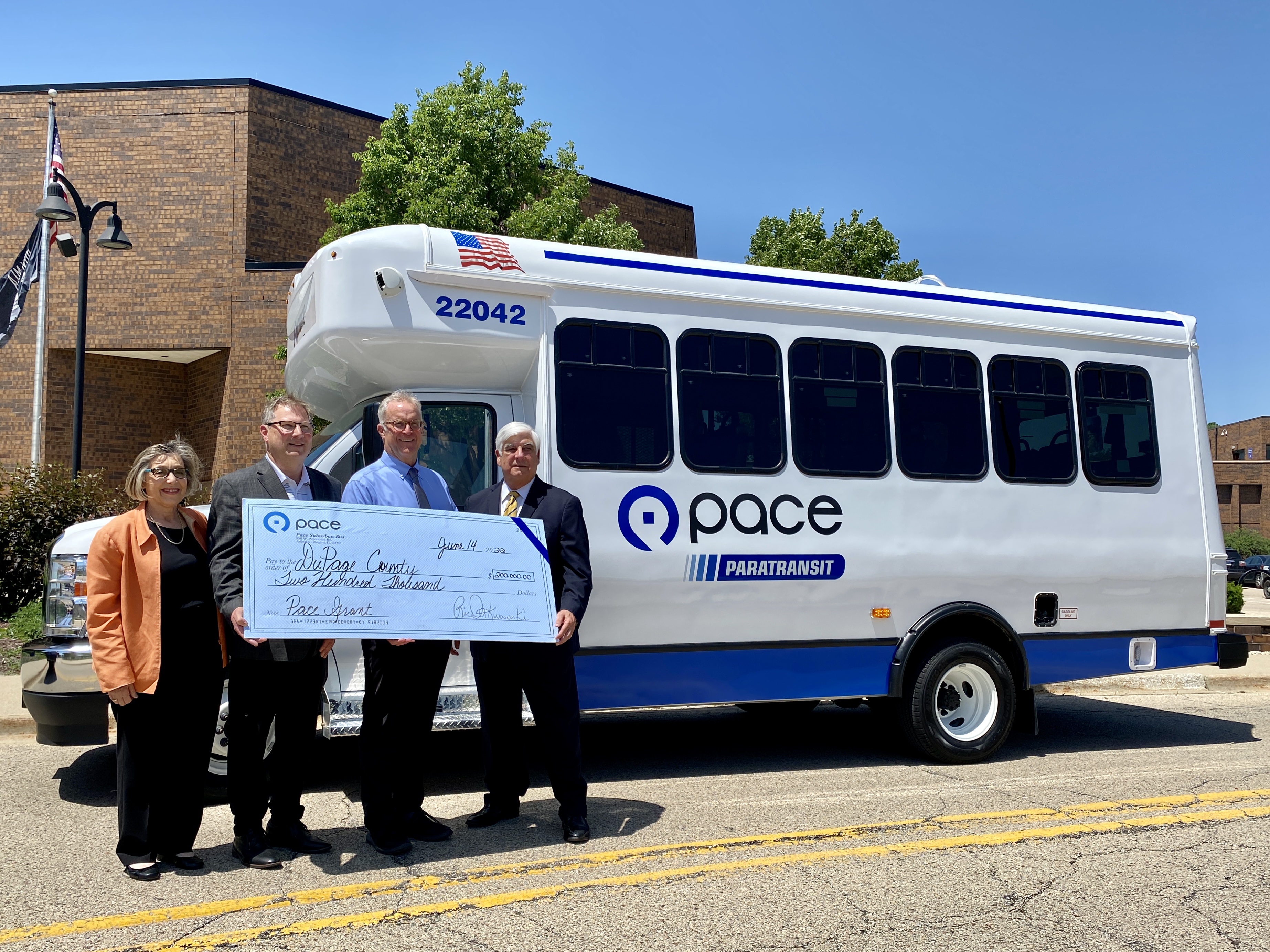 officials hold ceremonial check in front of paratransit bus