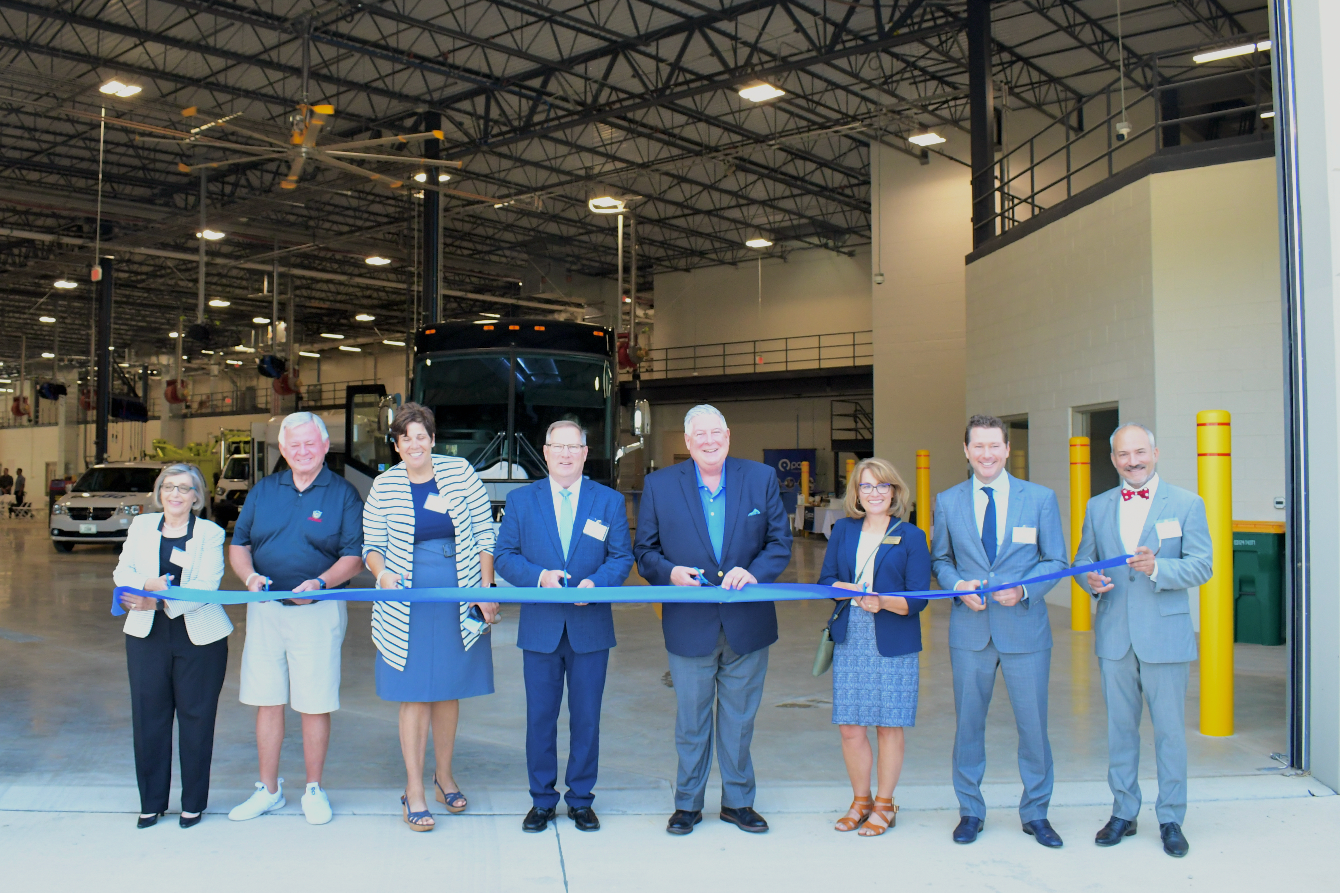 Officials pose with a long blue ribbon at bus garage entrance