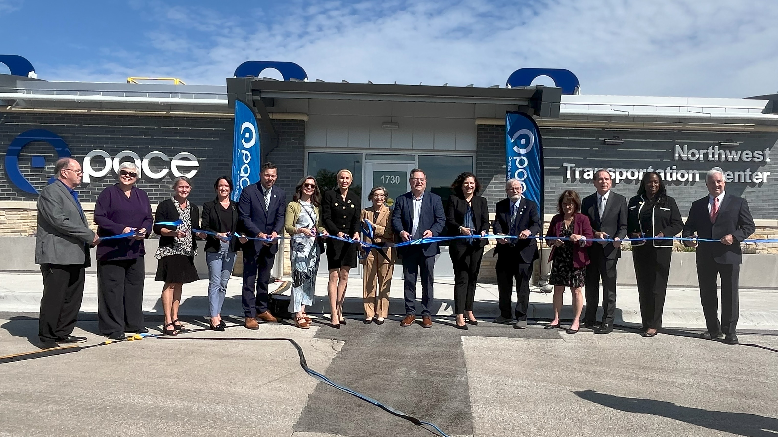 Photo of local, state, and Pace officials standing in front of a passenger waiting area at the Northwest Transportation Center in Schaumburg with a blue riboon in hand.