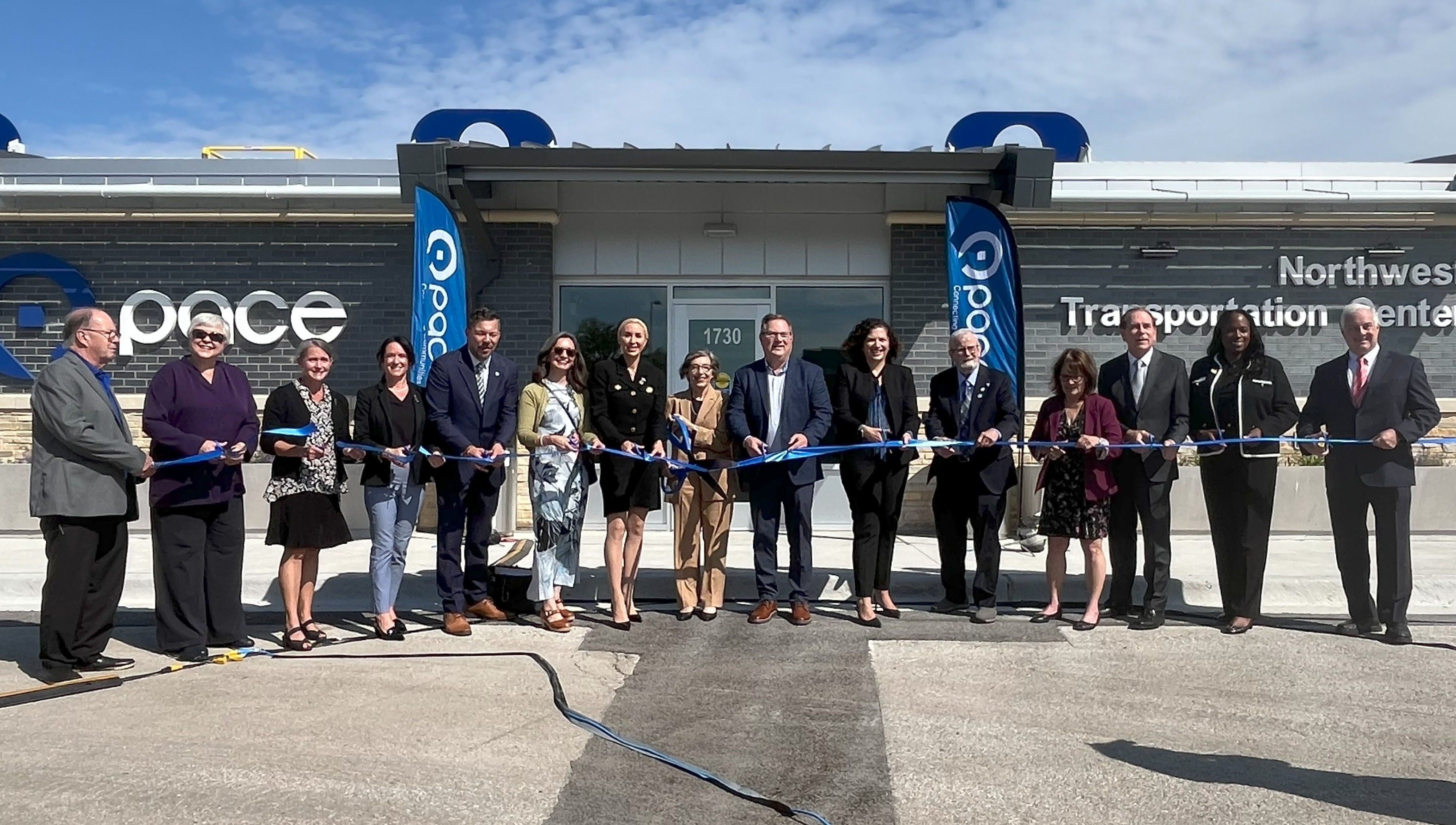 Photo of local, state, and Pace officials standing in front of a passenger waiting area at the Northwest Transportation Center in Schaumburg with a blue ribbon in hand.