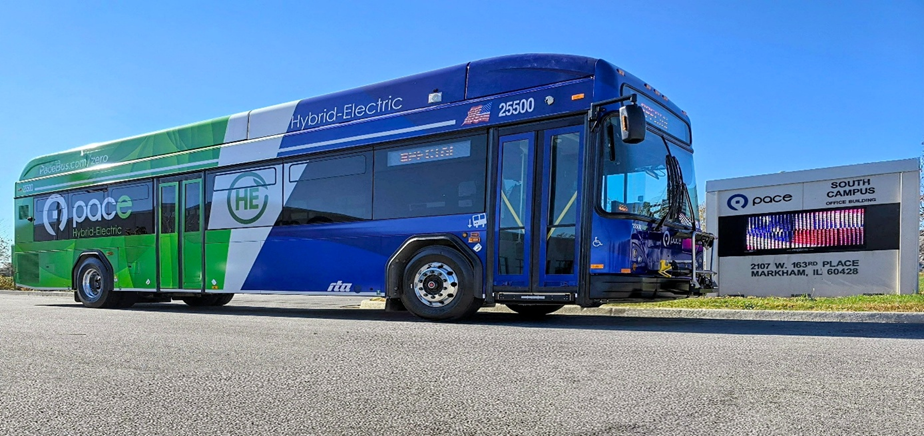 Hybrid electric bus in green, white, and blue colors parked outside and near a building sign