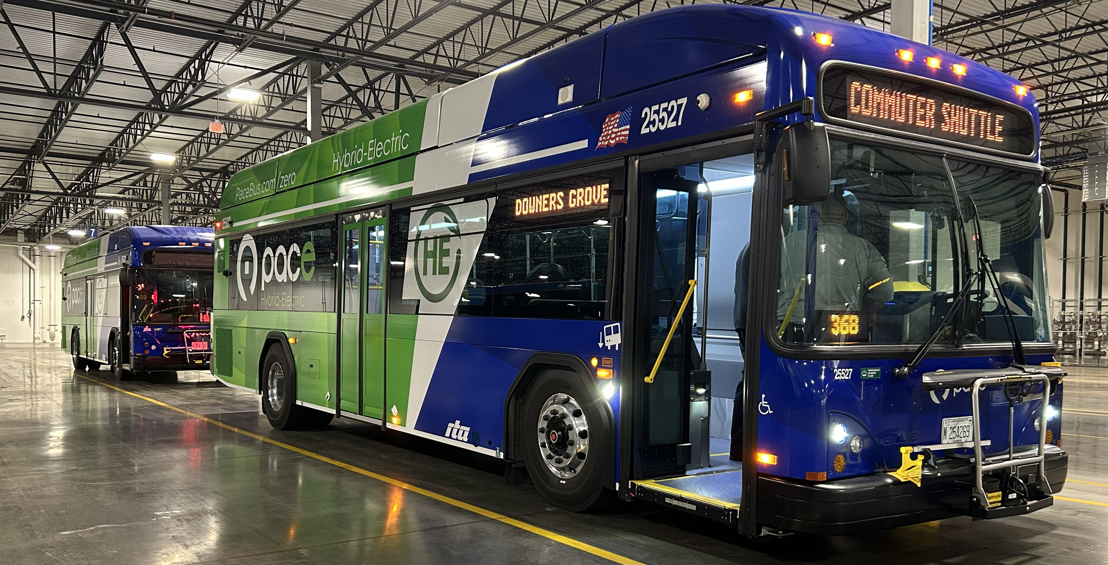 2 blue and green buses lined up inside garage with 'hybrid' logo