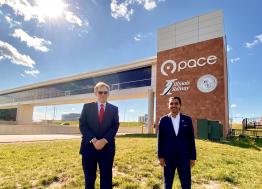 Two men in business suits stand in front of a pedestrian bridge with Pace logo