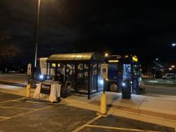 nighttime outdoor photo of Pace express bus at a bus stop shelter with a nearby display table
